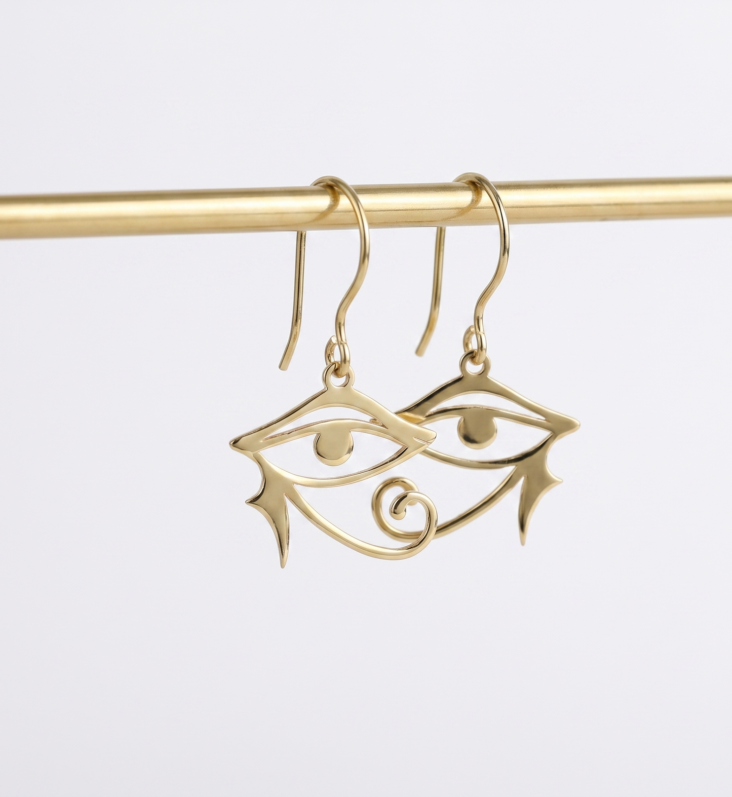 Gold eye-shaped earrings on a gold rod against a white background