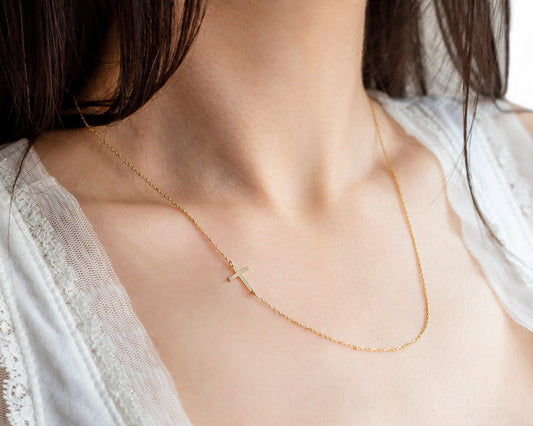 A woman wearing a white lace shirt showcasing a 14K gold sideways cross necklace.