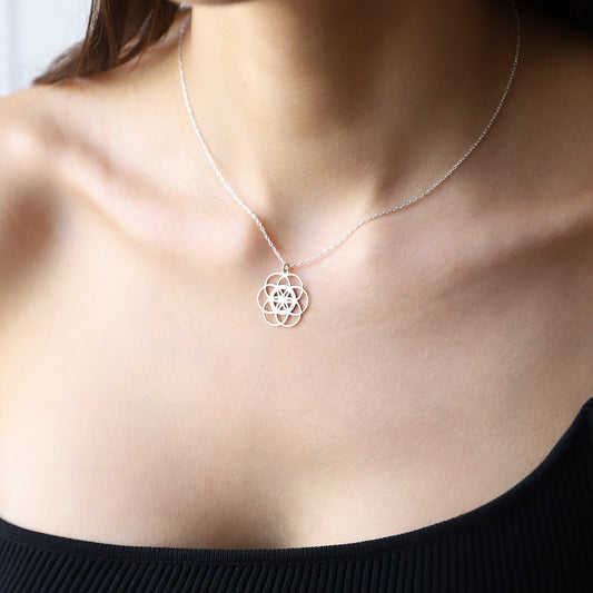 A person wearing a silver pendant necklace with a floral seed of life design.