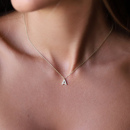 A close-up image of a woman wearing a custom dainty dangle pendant necklace with a pave initial design, in silver color.