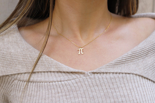 A woman wearing a dainty pendant necklace with the Pi symbol, in a gold-tone finish.