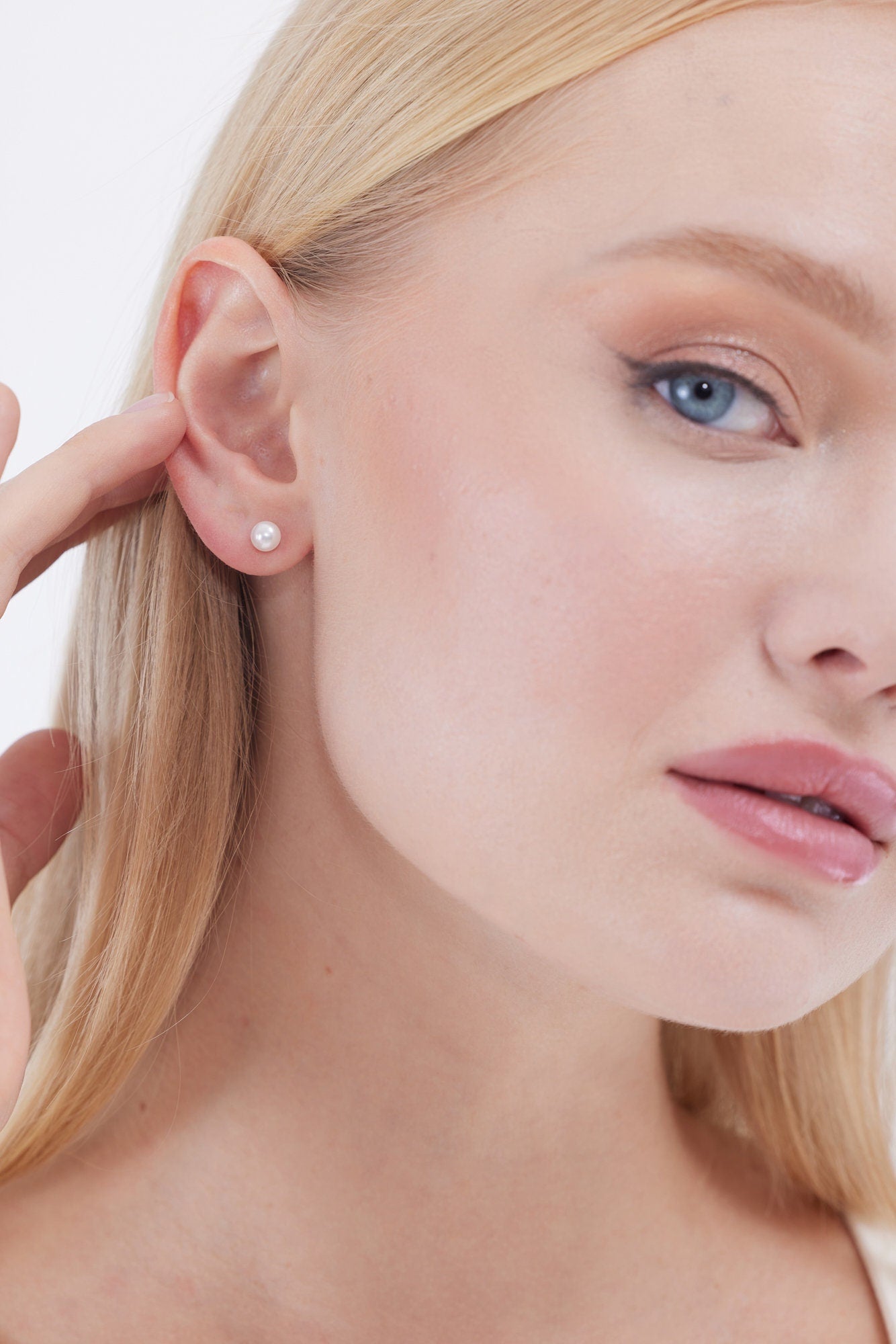 Close-up of a woman wearing pearl earrings with text 'SHIPS NEXT DAY' on a neutral background