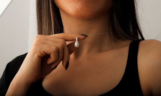 A person wearing a black top holding a dainty freshwater pearl necklace with a gold accent, showcasing its design.
