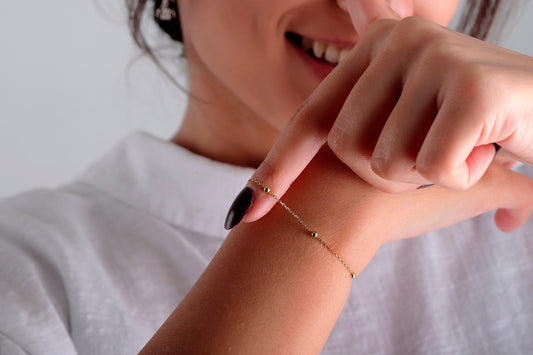 A woman's wrist wearing a dainty 14K gold satellite chain bracelet.