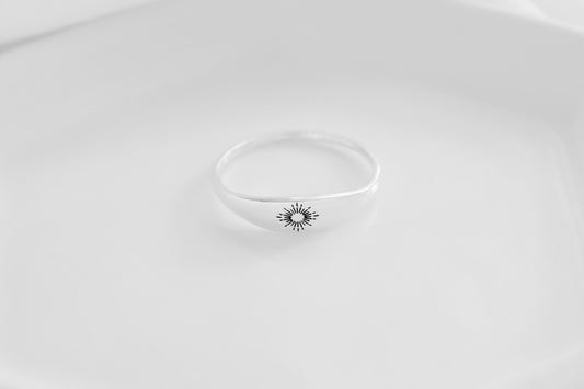 A minimalistic sterling silver ring with a sunburst design on a white background.