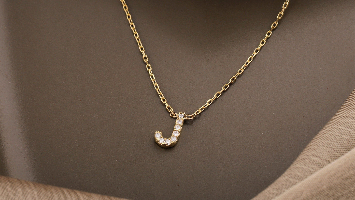 Gold necklace with a 'J' pendant on a brown background