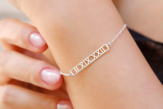 A sterling silver bar bracelet with Roman numerals engraved on it, worn on a person's wrist.
