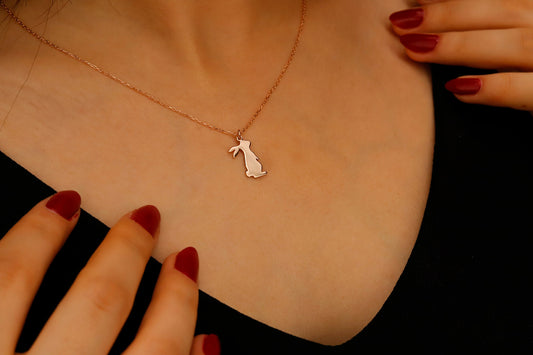 Rose gold necklace with a small pendant on a person's neck against a black background