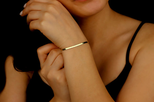 A close-up image of a woman's wrist wearing a gold italian snake herribhbone flat chain bracelet.
