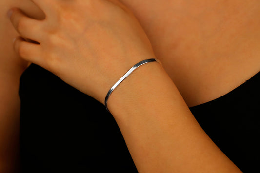 A close-up image of a woman's wrist wearing a silver flat snake chain bracelet.
