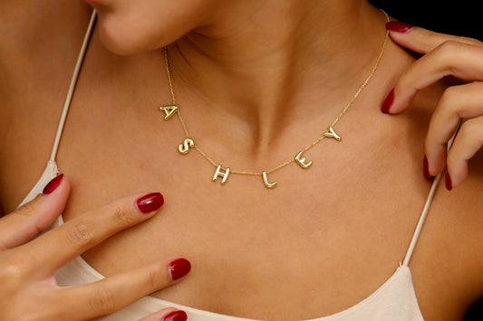 Gold necklace with 'SHLEY' pendant on a person wearing a white top.