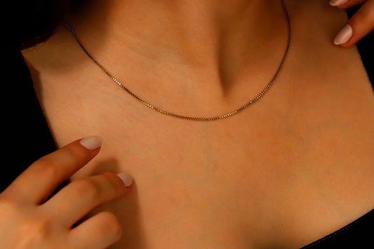 A close-up image of a gold box chain necklace with delicate layered chains, displayed on a person's neck.