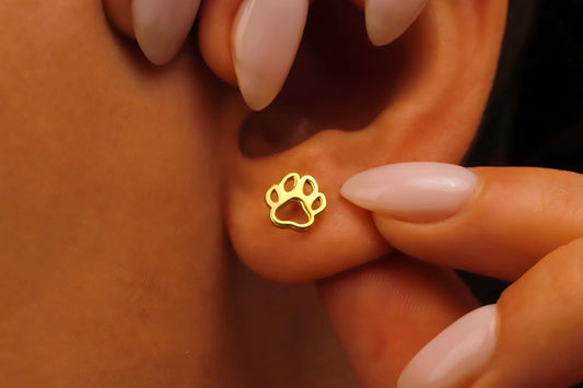 Gold paw print earring being worn on a person's ear.