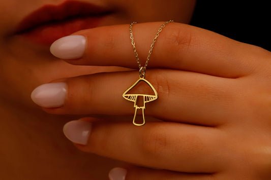 A close-up image of a person's hand holding a dainty gold necklace with a mushroom pendant.