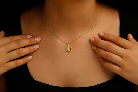 Gold necklace with a sunflower pendant worn by a person against a dark background