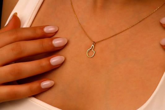 A close-up image of a person wearing a tiny middle finger-shaped necklace in silver, with hands adjusting the necklace.