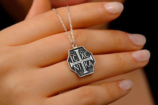 Silver necklace with a hexagonal pendant on a hand against a dark background