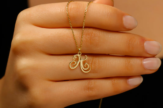Gold necklace with a 'K' pendant held in a hand against a neutral background