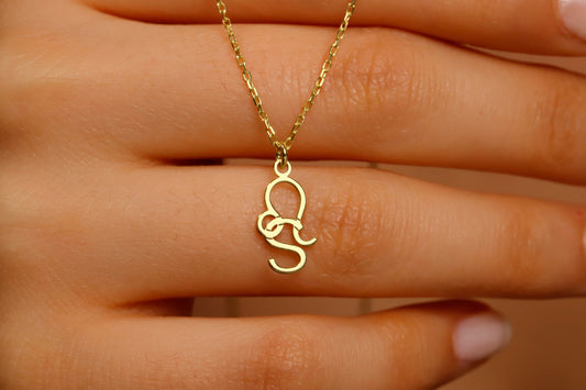 Gold necklace with a unique pendant held by a hand against a neutral background