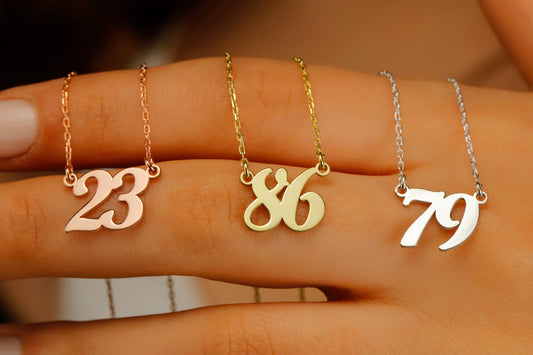 Three dainty necklaces with numbers '23', '86', and '79' displayed on a person's finger, indicating different lucky numbers or birth years.