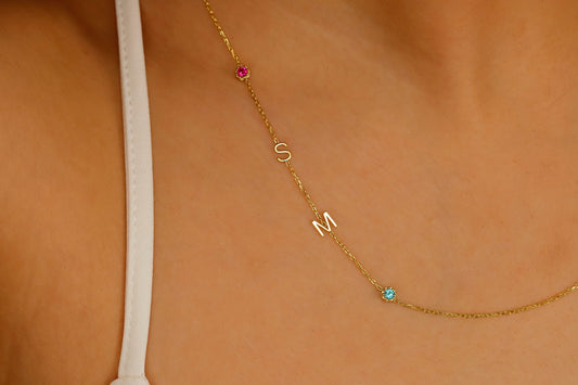 A close-up image of a sterling silver necklace with gold lettering and multicolored birthstones laid out on a person's neck.