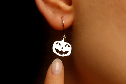 Silver jack-o'-lantern earring on a person's ear with a dark background