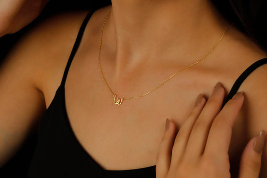 A woman wearing a black tank top showcasing a silver necklace with Arabic script.
