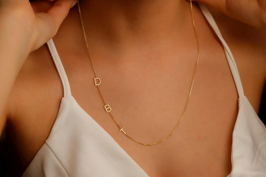 A close-up image of a custom Sideway Initial Necklace worn on a person's neck, displaying gold letters on a chain.