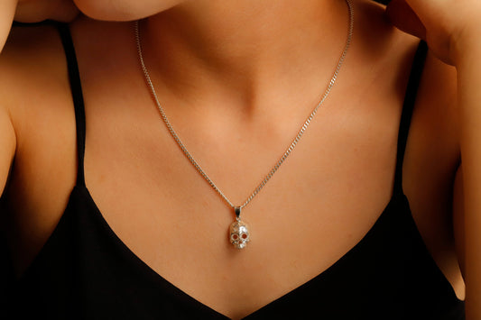 A close-up image of a person wearing a minimalist skull charm necklace with a gold chain and a small skull pendant.