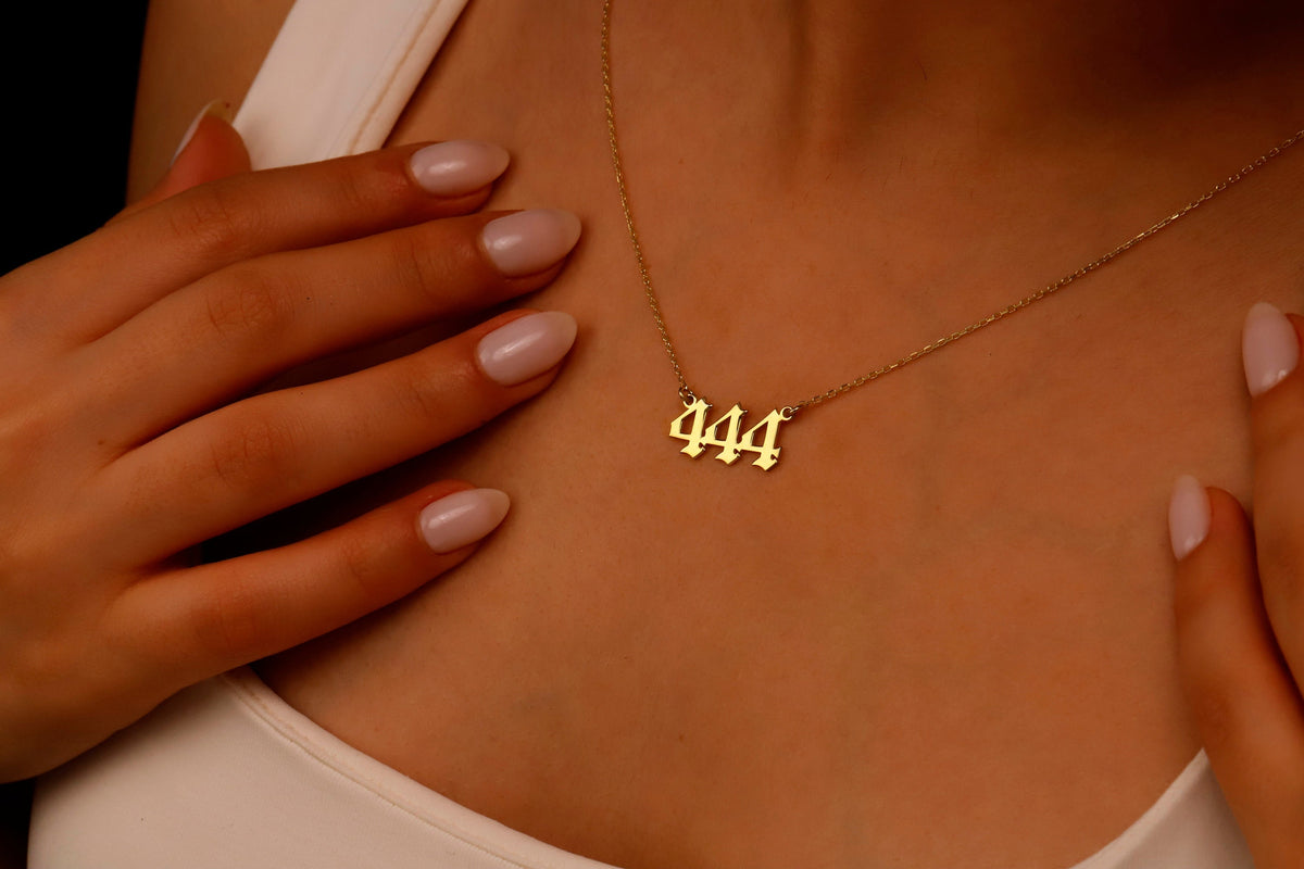 A close-up image of a necklace with the number 444 on a charm, held by a person with red nail polish.