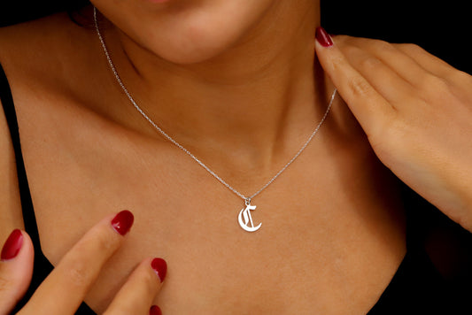 A close-up image of a woman wearing a sterling silver necklace with a gothic style initial pendant.