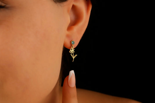 A close-up image of a woman's ear wearing a dangle birth month flower earring with a birthstone.