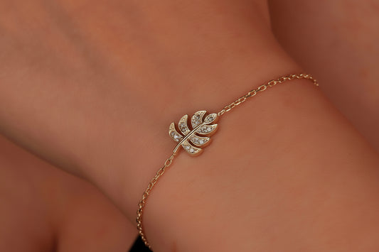 A gold-colored bracelet with a monstera deliciosa leaf pendant, featuring CZ stones, displayed on a person's wrist.