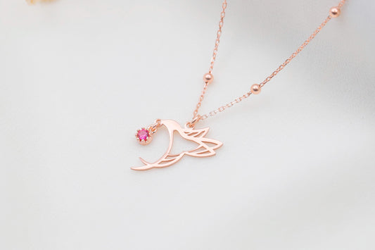 A close-up image of a rose gold-colored necklace with a bird charm and beaded ball chain.