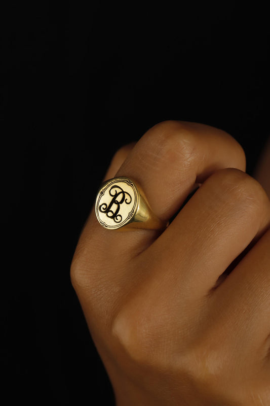 A person's hand displaying a gold-filled signet ring with an engraved single letter monogram.