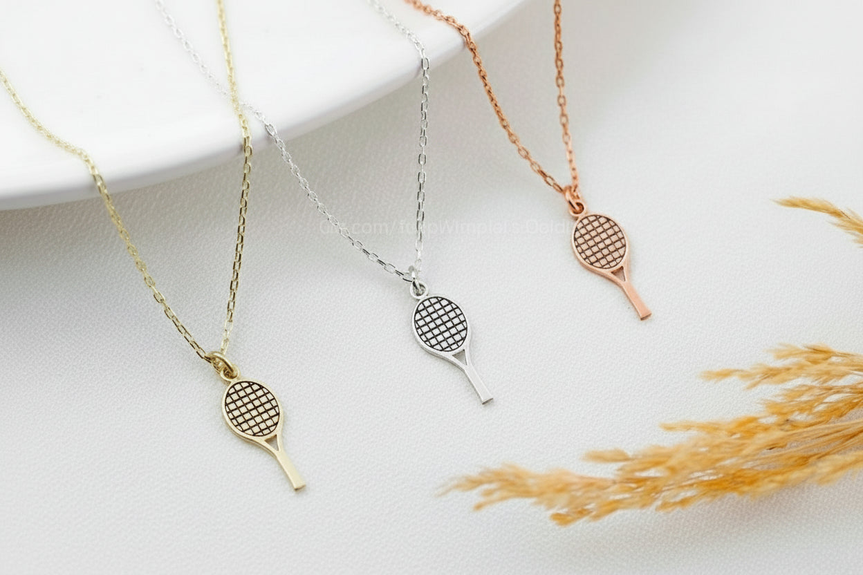Three tennis racket necklaces in gold, silver, and rose gold on a white background with dried grass.