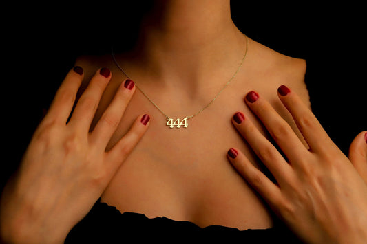 A close-up image of a necklace with the number '444' on a charm, held by a person with red nail polish.