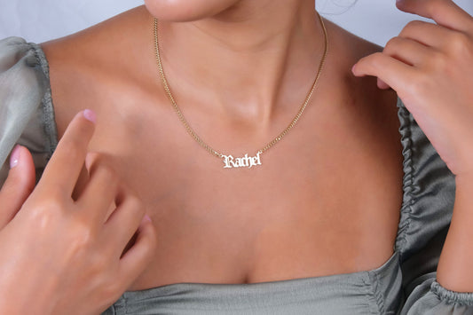 A close-up image of a woman wearing a gold-filled name necklace with a curb chain design.