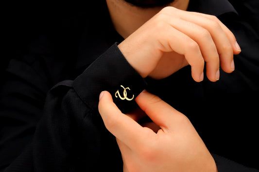 A close-up image of a man's hand holding a personalized cufflink with a monogram initial on it.
