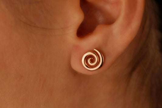 A close-up image of a person's ear wearing a gold-colored spiral stud earring.
