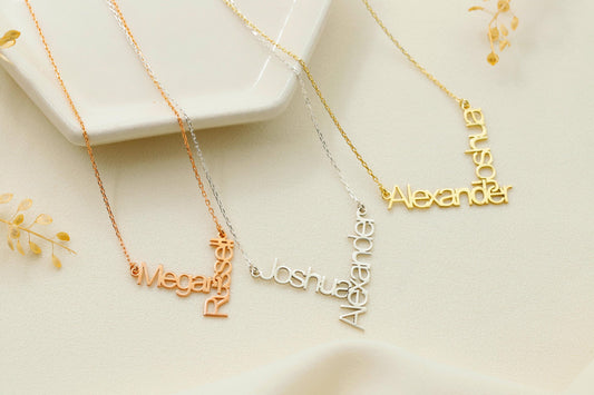 Three personalized name necklaces in silver, rose gold, and gold colors, each with a name written on them, displayed on a white surface with some decorative elements.