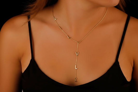 A model wearing a gold-colored lariat name necklace with bubble initial design.