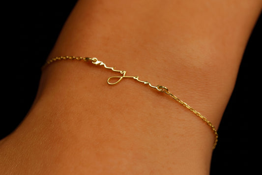 A close-up image of a gold personalized name bracelet on a person's wrist, featuring a delicate chain design and a custom initial pendant.