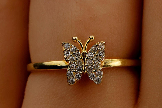Gold butterfly ring on a person's finger with a warm background