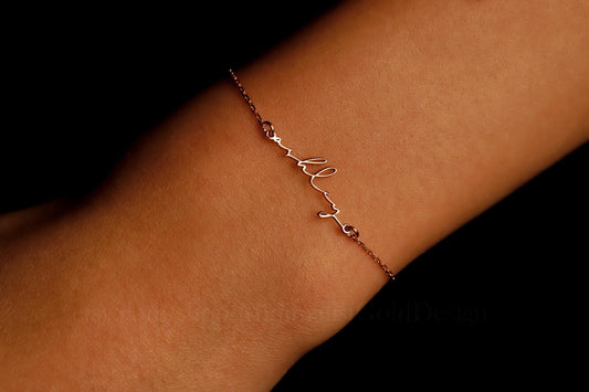 A personalized tiny name bracelet in 14K gold filled, featuring small text characters on a chain, worn on a person's wrist.
