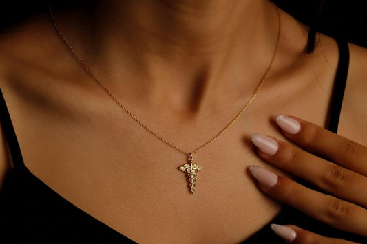 Gold necklace with a caduceus pendant on a person's neck