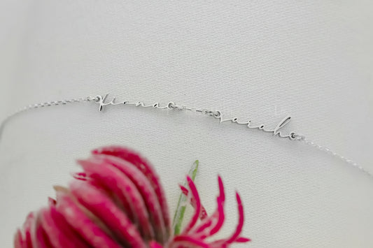 Silver necklace with 'forever love' engraving on a white background with pink flower.