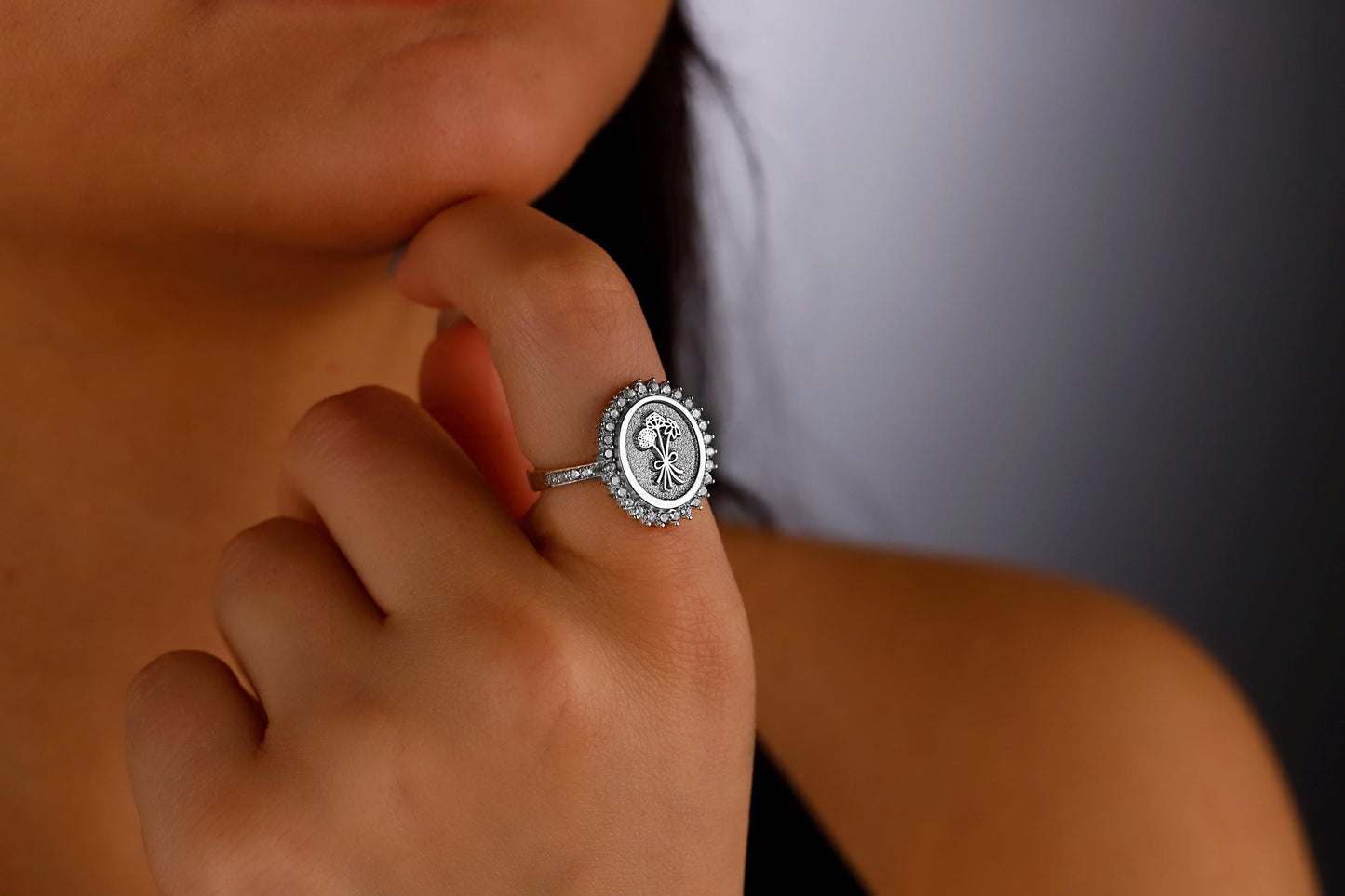 A close-up image of a silver ring featuring a birth flower design surrounded by multiple clear cubic zirconia stones.
