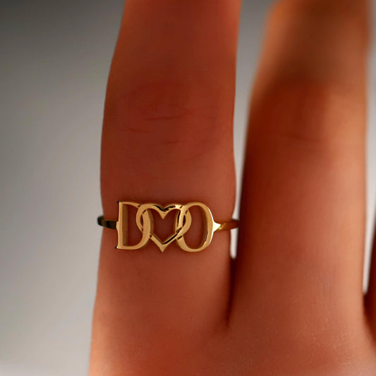 Gold ring with a unique design on a person's finger against a neutral background