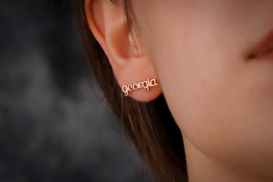 Gold earring with 'georgia' inscription worn by a person against a dark background
